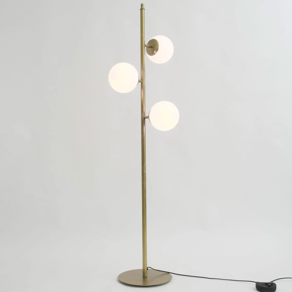 Lámpara de pie moderna con estructura metálica dorada y tres globos de luz blanca distribuidos verticalmente sobre un fondo neutro.