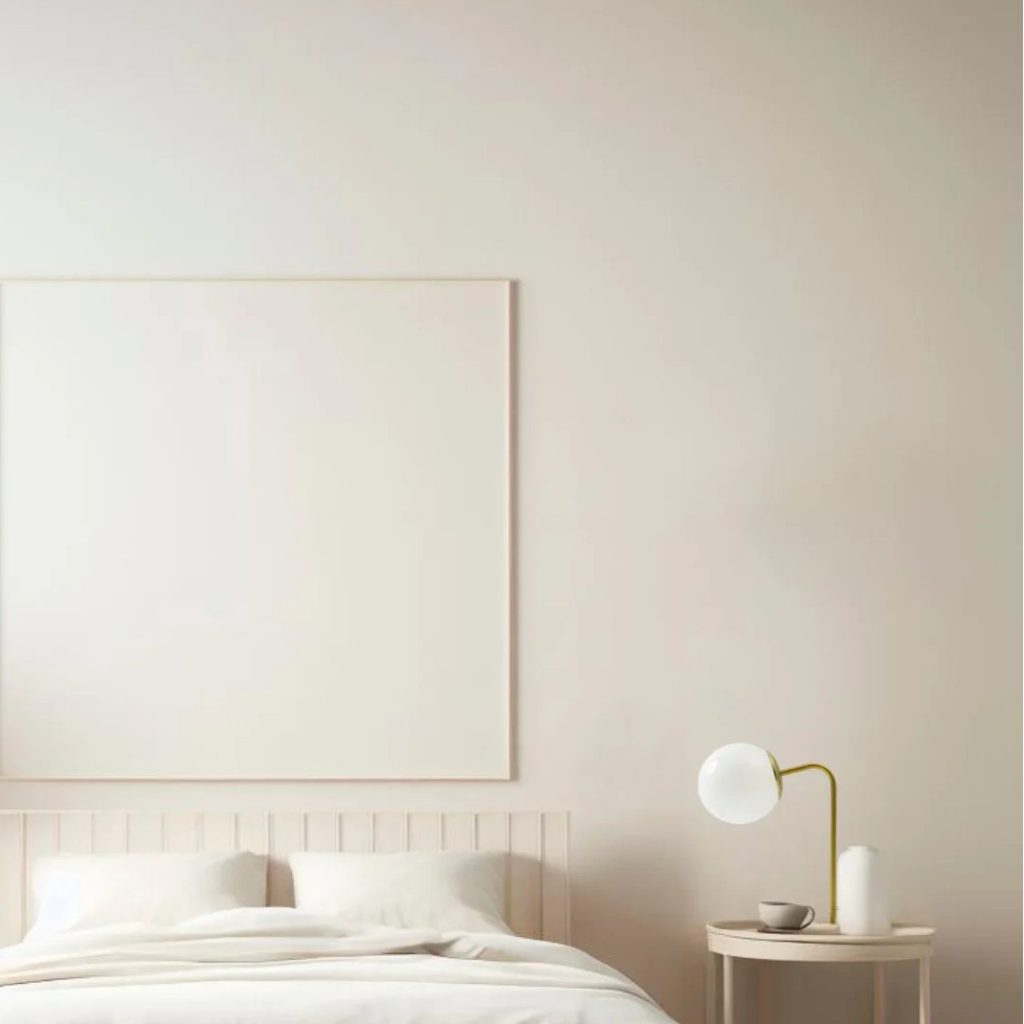 Lámpara de mesa con globo de cristal opal y base dorada sobre mesita junto a una cama blanca.