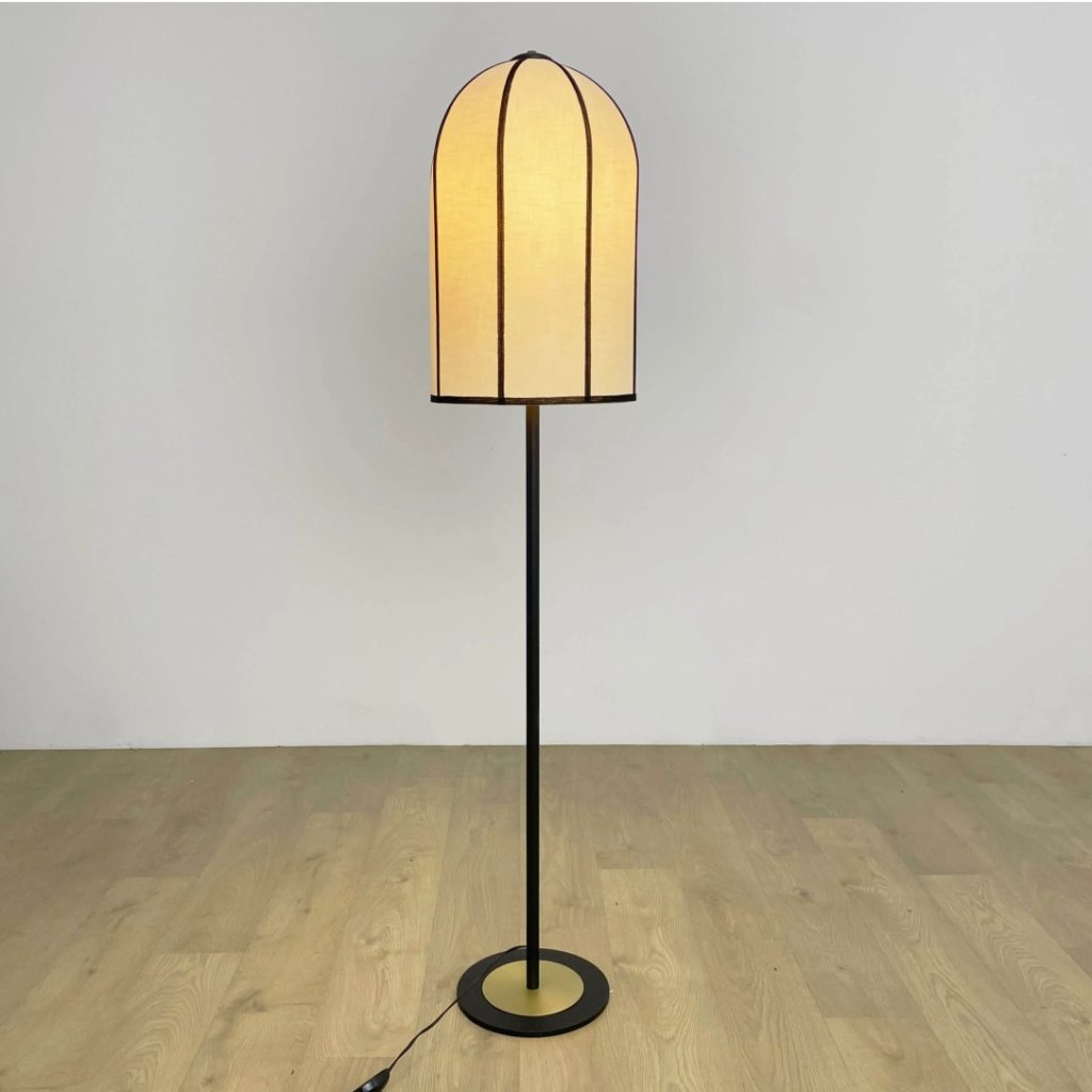 Lámpara de pie con pantalla de lino beige y estructura negra sobre suelo de madera.