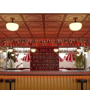 Bar de estilo retro con barra iluminada, taburetes y decoración en tonos rojos y cálidos.