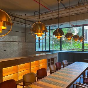Comedor moderno con lámparas colgantes metálicas doradas y luz cálida sobre una mesa larga en ambiente industrial.