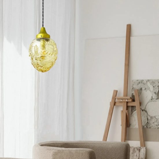 Lámpara colgante de cristal ámbar con motivos florales en un interior luminoso y de estilo minimalista.