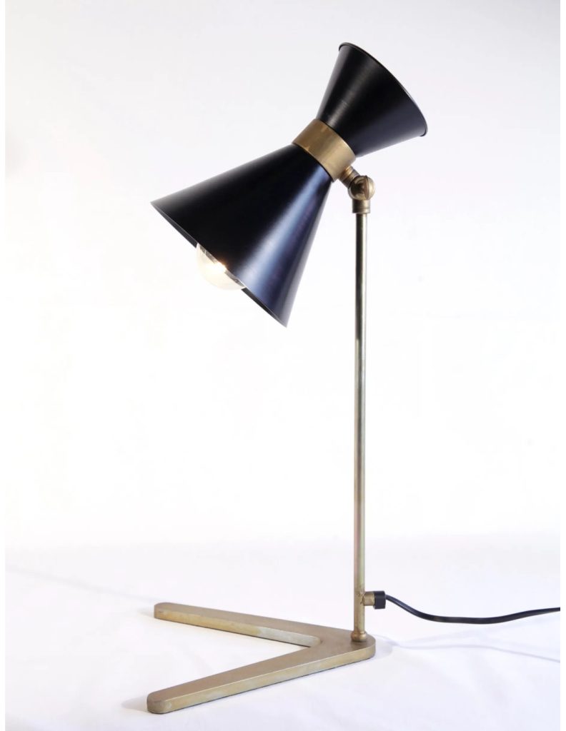 Lámpara de mesa negra con pantalla doble tipo diabolo, estructura metálica dorada y base geométrica sobre fondo blanco.