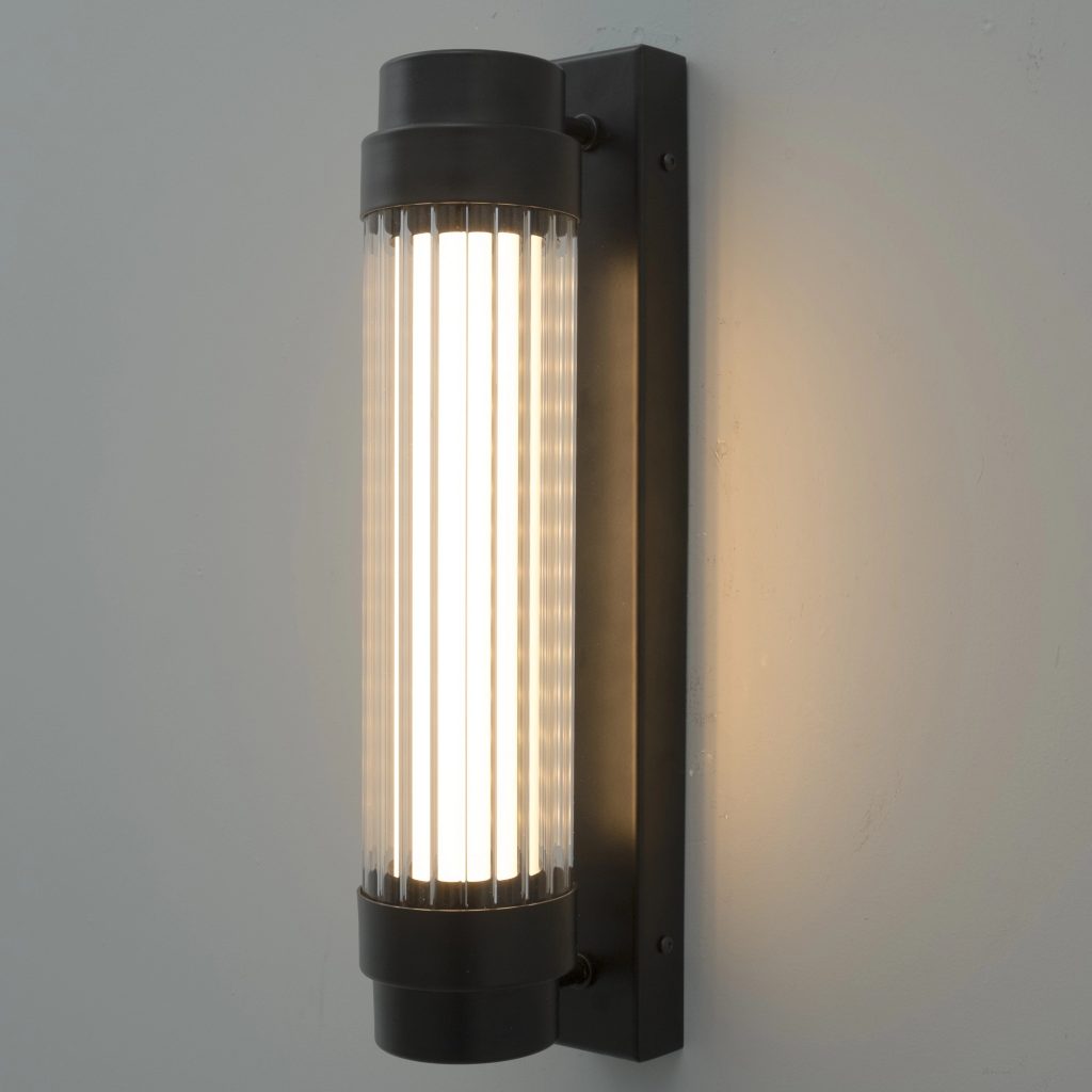Aplique de pared cilíndrico con acabado negro y difusor acanalado que emite luz cálida.
