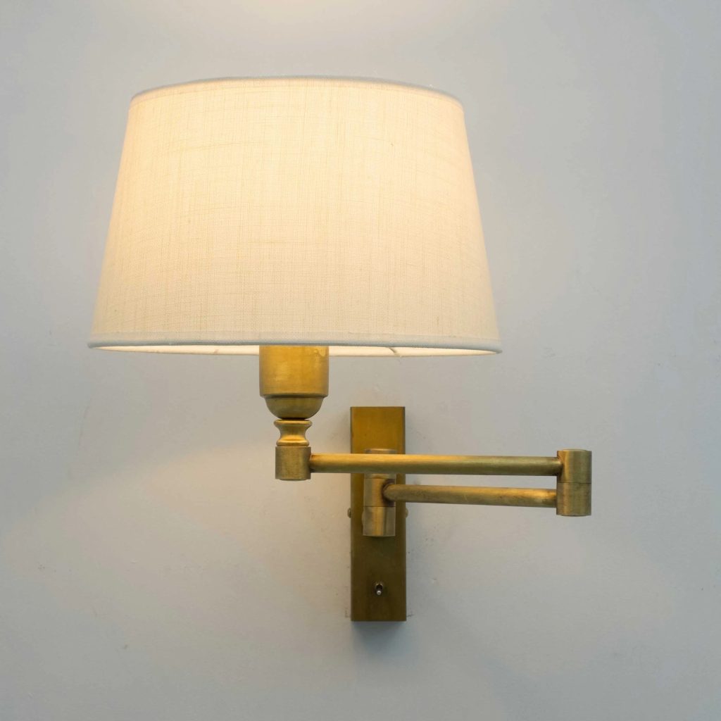 Aplique de pared vintage articulado en latón con pantalla de tela beige e iluminación cálida.