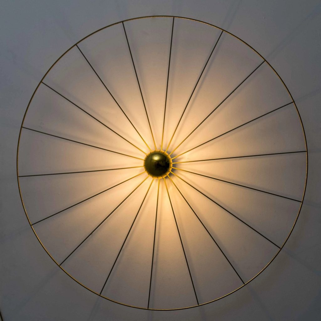 Aplique de pared vintage circular con estructura metálica tipo sol, varillas radiales y luz cálida decorativa.