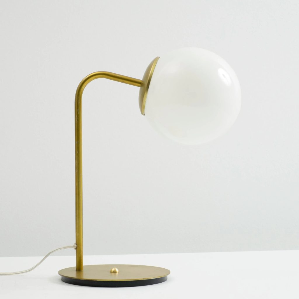 Lámpara de sobremesa con estructura metálica dorada y pantalla esférica de vidrio blanco.