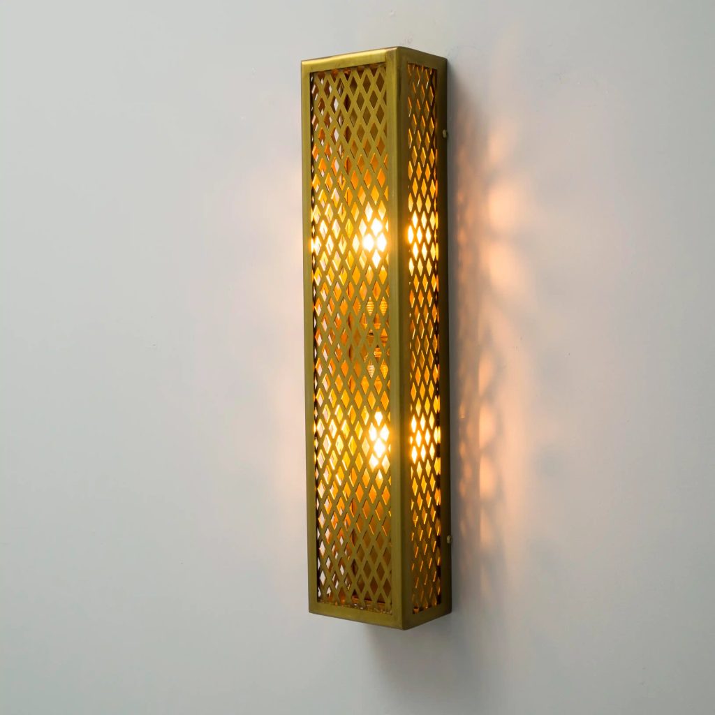Aplique de pared vertical en latón con rejilla metálica e iluminación cálida de estilo industrial.