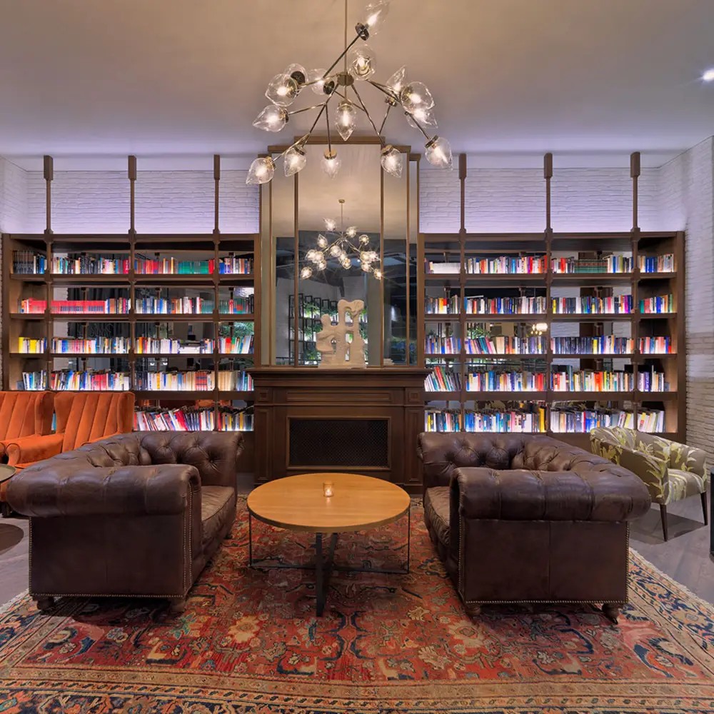 Elegante salón biblioteca con lámpara colgante escultórica de brazos metálicos y tulipas de cristal decorativo.