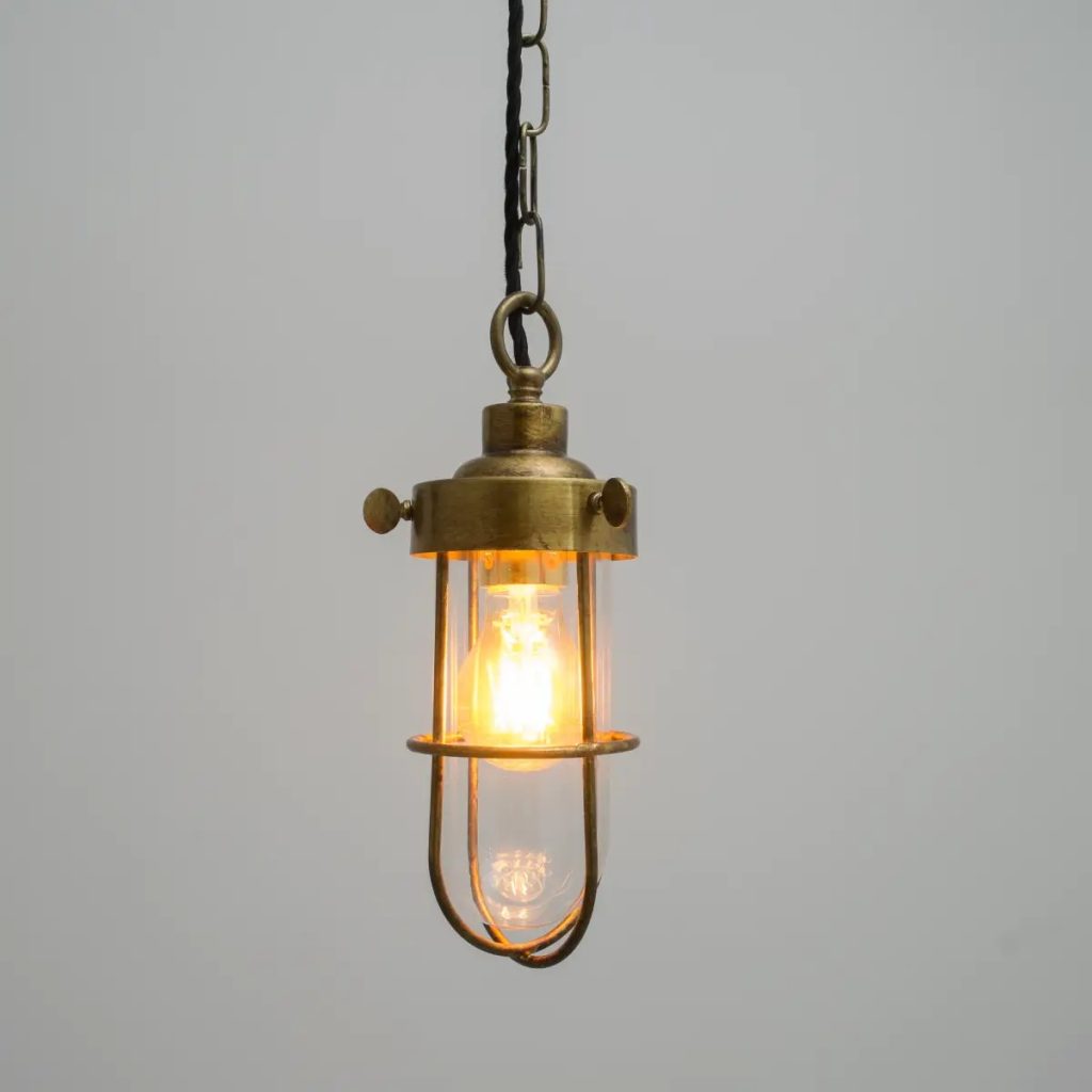 Lámpara colgante industrial de latón envejecido con cristal transparente y bombilla vista.
