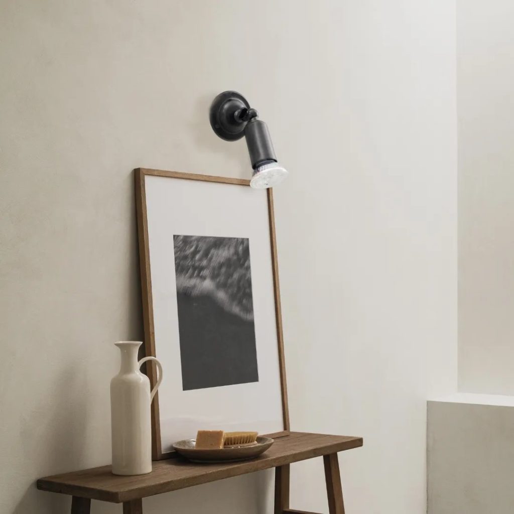 Aplique de pared orientable en acabado negro iluminando un cuadro sobre una repisa de madera.