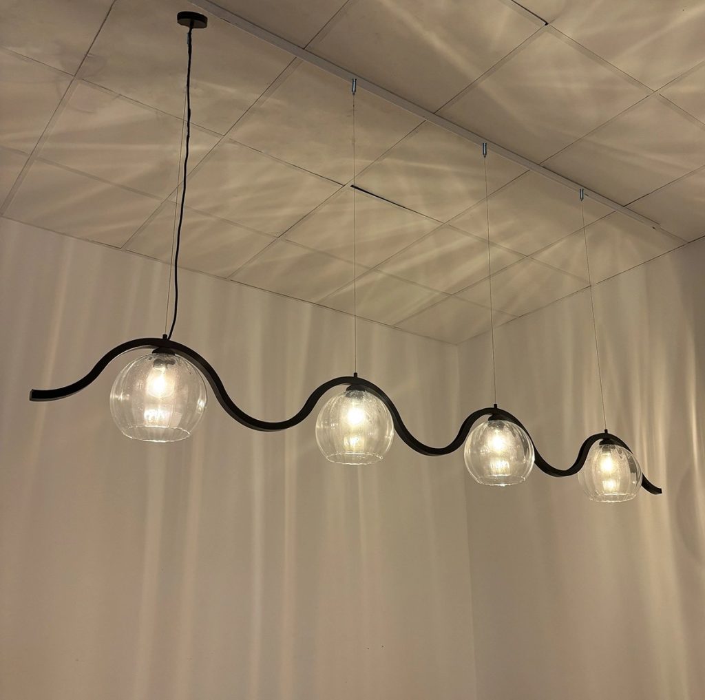 Lámpara colgante lineal con estructura ondulada negra y cuatro tulipas de cristal transparente.