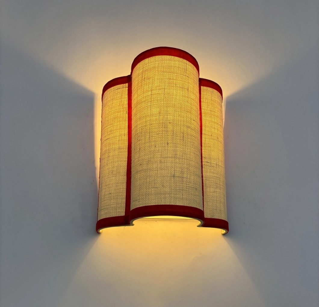Aplique de pared con pantalla textil beige y ribetes rojos que emite una luz cálida y envolvente.