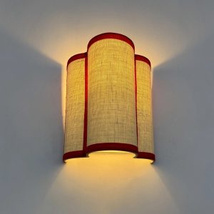 Aplique de pared con pantalla textil beige y ribetes rojos que emite una luz cálida y envolvente.