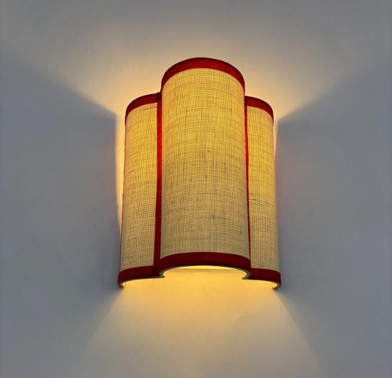 Aplique de pared con pantalla textil beige y ribetes rojos que emite una luz cálida y envolvente.