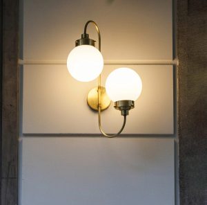 Aplique de pared con doble esfera opal y estructura en latón envejecido iluminando un interior elegante.