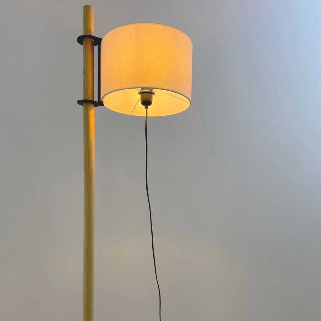 Lámpara de pie con estructura de madera y pantalla cilíndrica textil que emite luz cálida.