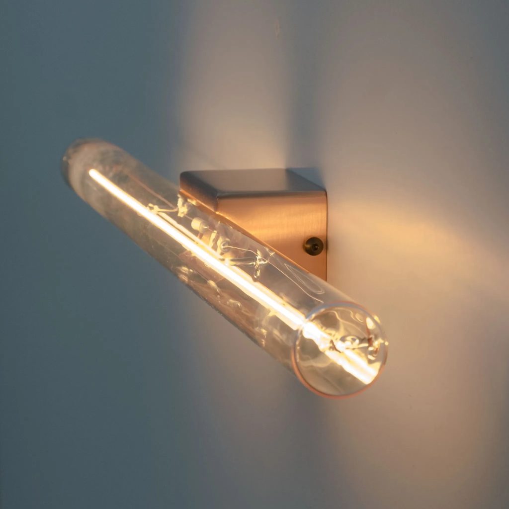 Aplique de pared vintage con bombilla tubular LED vista, base metálica dorada e iluminación cálida decorativa.