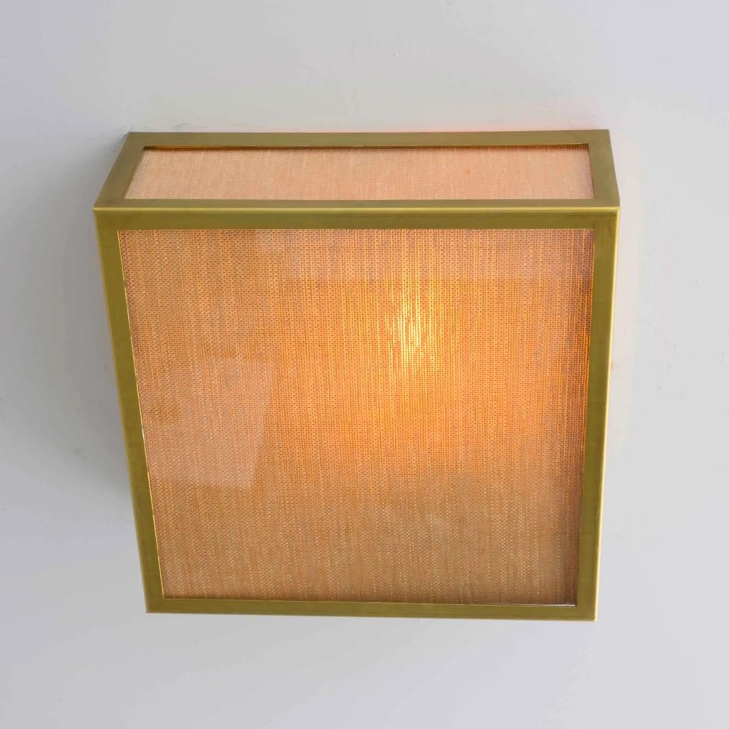 Plafón de techo rectangular con estructura en latón y pantalla textil beige iluminada con luz cálida.