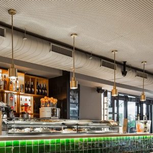 Lámparas colgantes cilíndricas de latón instaladas sobre barra de bar con azulejos verdes.