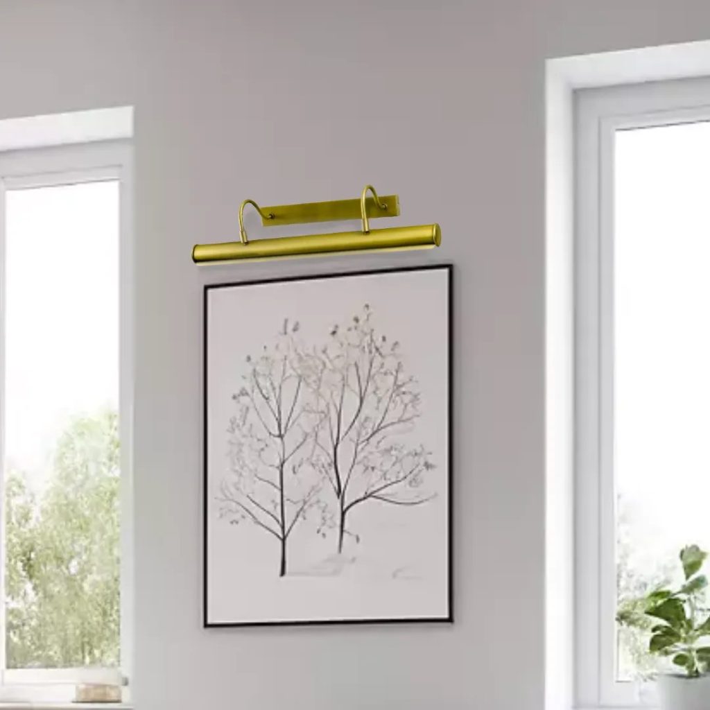 Iluminacuadros vintage dorado instalado sobre lámina decorativa, ideal para destacar obras de arte, cuadros y paredes elegantes.