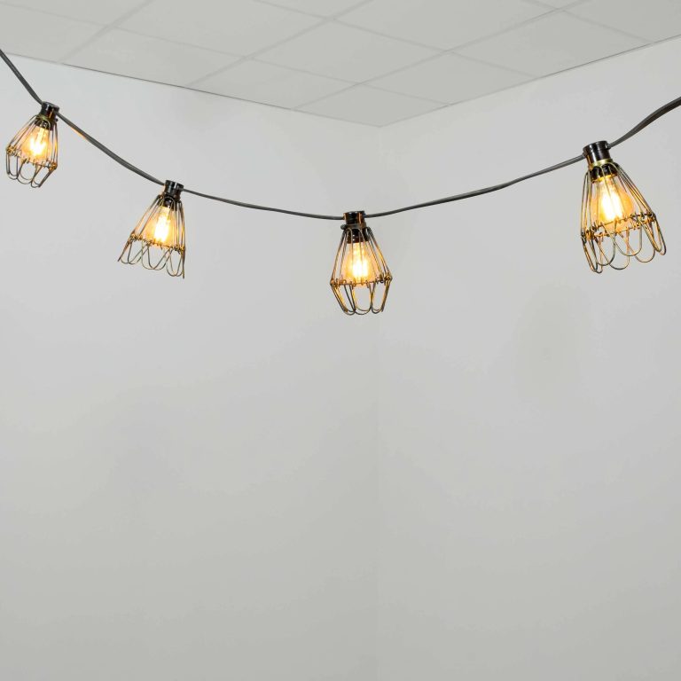 Guirnalda luminosa vintage con bombillas cálidas y pantallas metálicas tipo jaula suspendidas en cable negro.