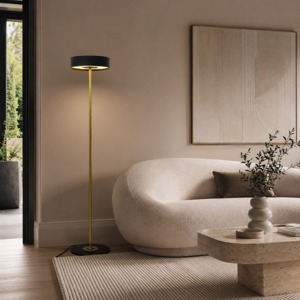 Lámpara de pie moderna en negro y dorado junto a sofá curvo beige en salón elegante de tonos neutros.