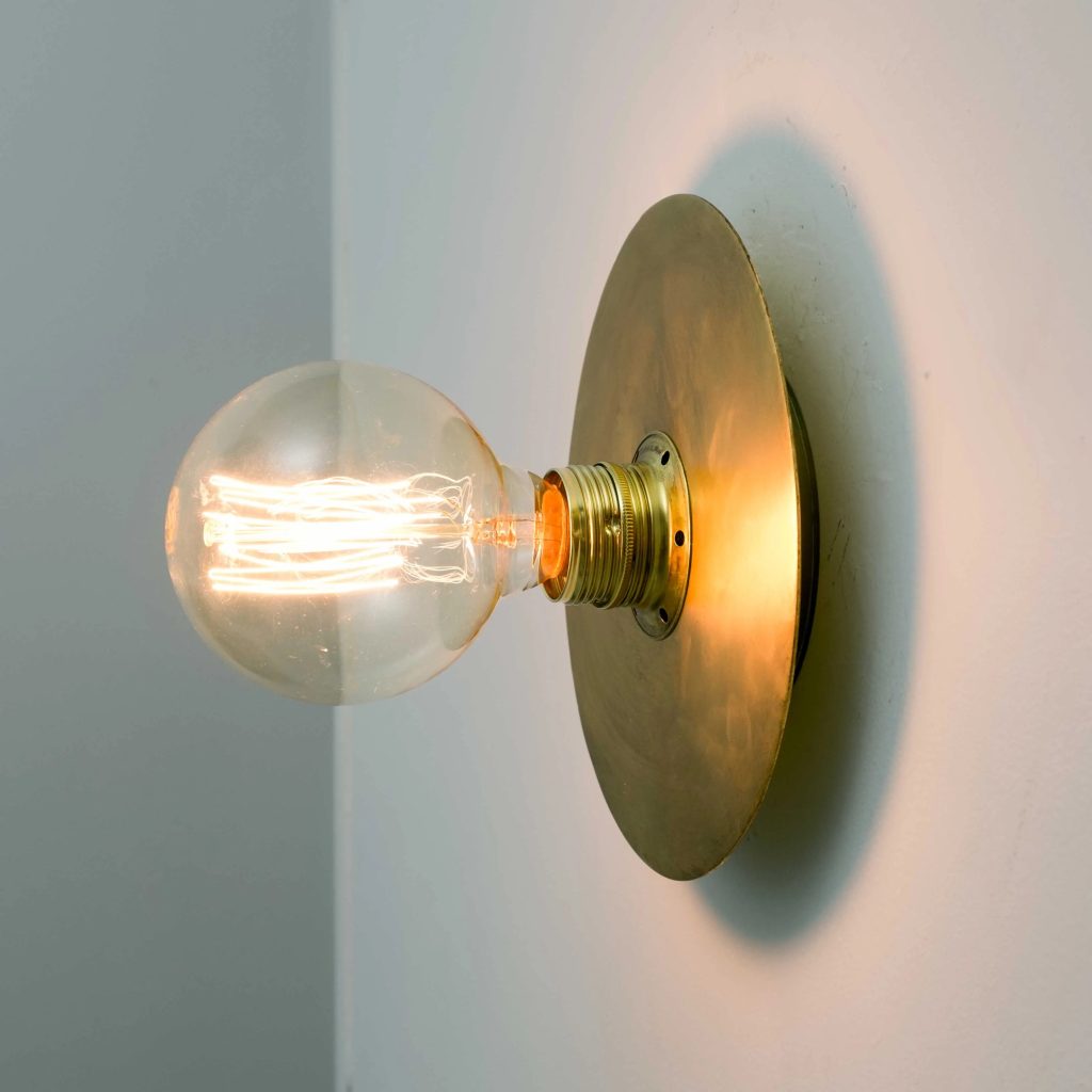 Aplique de pared vintage en latón con bombilla Edison vista iluminada con luz cálida.