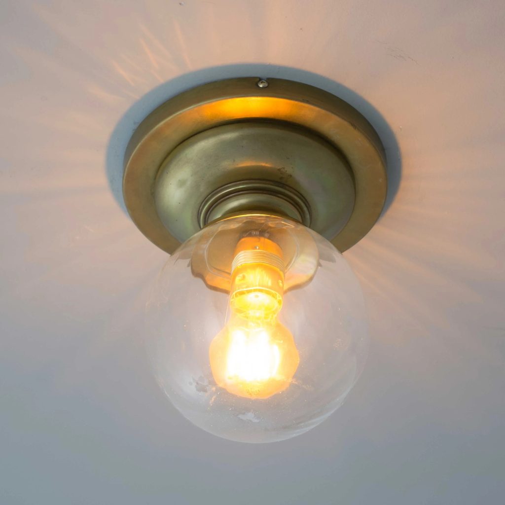 Plafón de techo vintage en latón envejecido con globo de cristal transparente y bombilla cálida vista.
