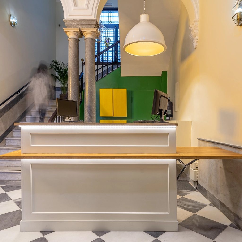 Lámpara colgante industrial blanca iluminando el mostrador de recepción de un edificio con columnas y suelo de mármol.