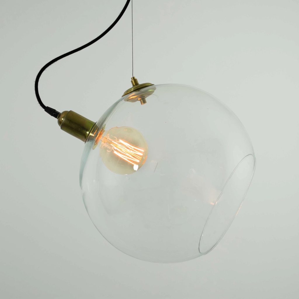Lámpara colgante con globo esférico de cristal transparente, portalámparas dorado y bombilla de filamento encendida.
