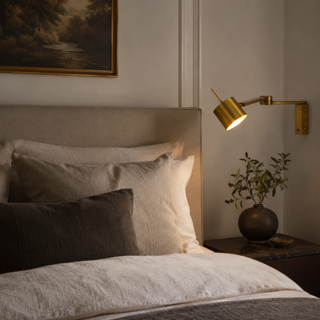 Aplique de pared articulado en latón instalado junto a cama, ideal como luz de lectura en dormitorio elegante.