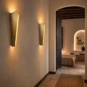 Dos apliques de pared verticales dorados con luz cálida ascendente y descendente en un pasillo de estilo mediterráneo.