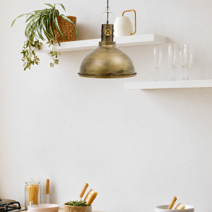 Lámpara colgante vintage industrial con pantalla de campana en acabado dorado rústico sobre pared blanca con estantes decorativos