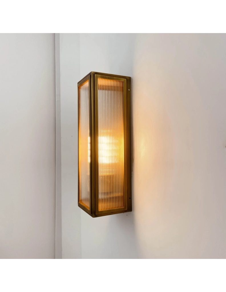 Aplique de pared vintage rectangular con cristal acanalado y acabado bronce iluminado sobre pared blanca