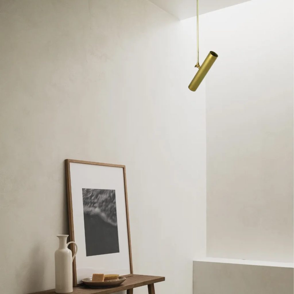 Lámpara colgante tubular de latón con diseño minimalista instalada en un interior de tonos neutros.