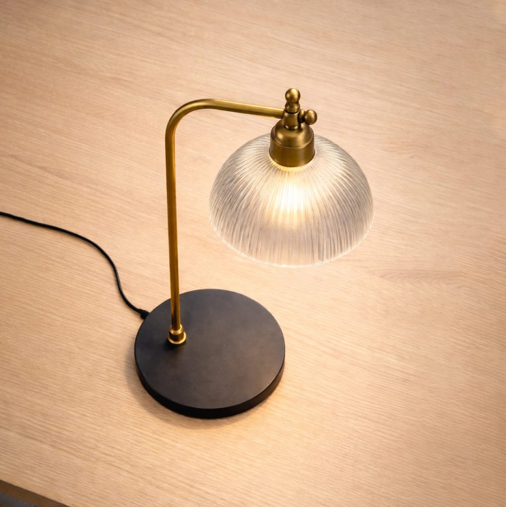 Lámpara de mesa vintage con base negra, estructura de latón y pantalla semiesférica de cristal estriado.
