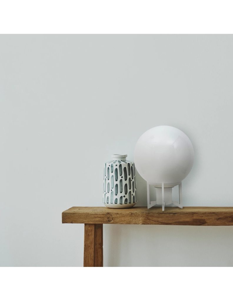 Lámpara de mesa vintage con esfera de cristal opal y estructura metálica blanca sobre una consola de madera.