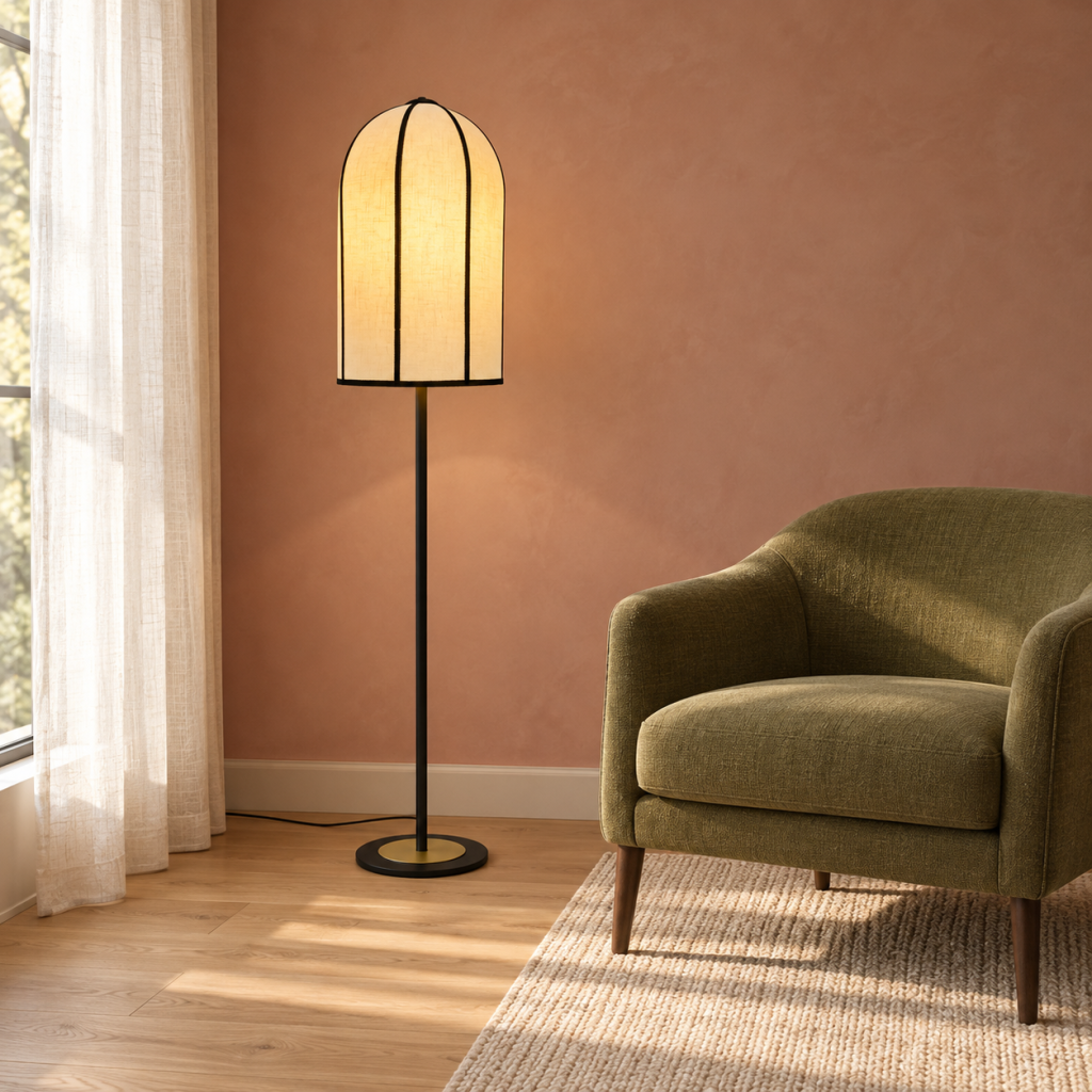 Lámpara de pie Gannon encendida, con pantalla de lino ribeteada en negro, junto a una butaca verde oliva y una pared rosa.
