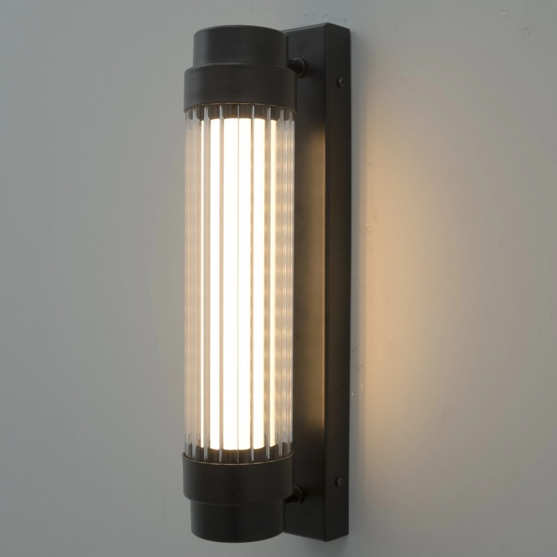 Aplique de pared negro con difusor de vidrio estriado iluminado en diseño vertical.