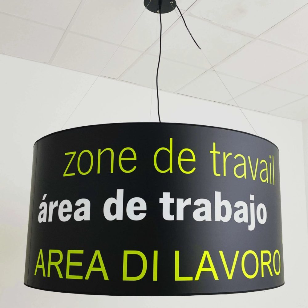 Lámpara colgante de pantalla cilíndrica negra personalizada con texto multilingüe, suspendida del techo.