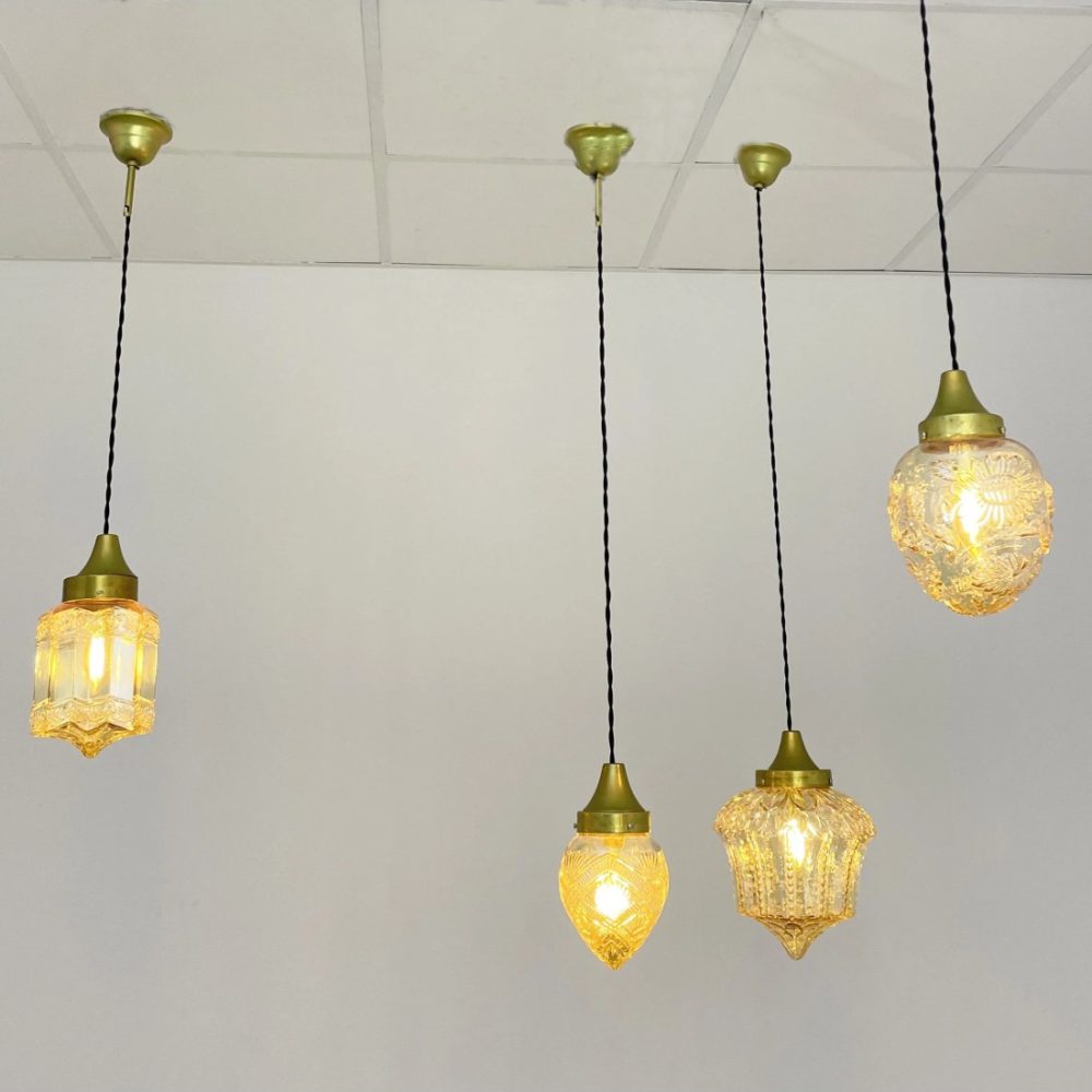 Conjunto de lámparas colgantes de cristal ámbar con diseños artesanales y luz cálida, suspendidas en un espacio interior.